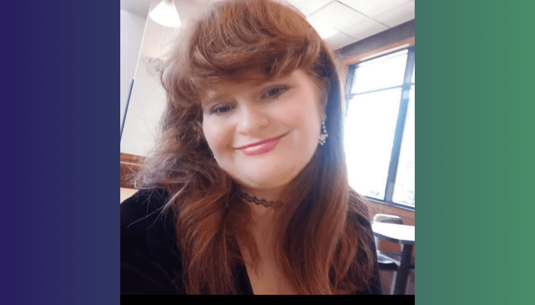 Smiling woman with long reddish hair and bangs wearing a black choker and earrings.