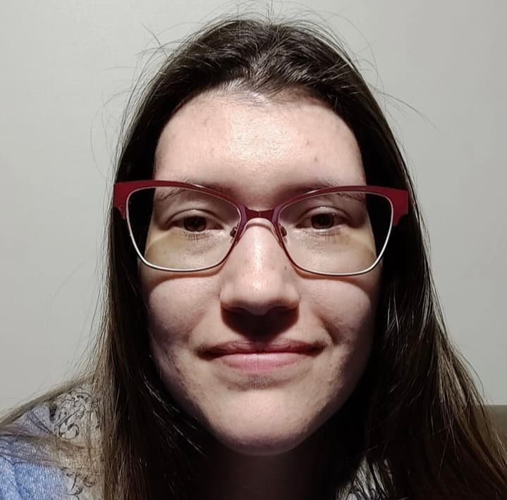 Close-up of a smiling woman with long brown hair wearing red-rimmed cat-eye glasses.