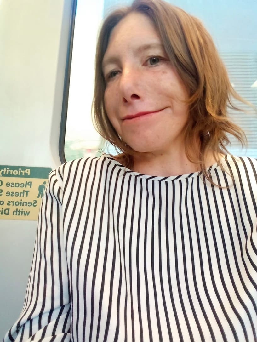 Smiling woman with auburn hair wearing a black and white striped shirt on a train.