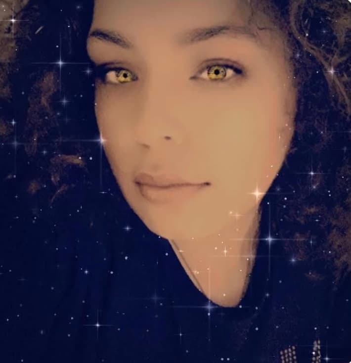 Woman with curly hair and striking yellow eyes, overlaid with a shimmering starry filter.
