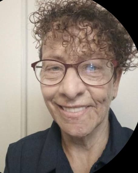 Smiling woman with short curly hair and glasses, wearing a dark blue collared shirt.